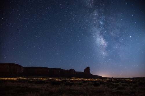 A starry night sky with the Milky Way over a desert landscape and silhouetted rock formations.