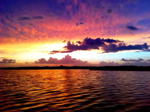 A vibrant sunset over a calm lake, with colorful clouds reflecting on the water's surface.