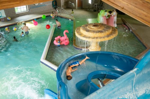 A vibrant indoor pool area with children playing, a water slide, and colorful inflatable toys.