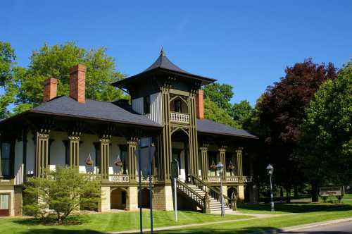 A historic building with a unique architectural style, featuring a tower, large windows, and lush green surroundings.