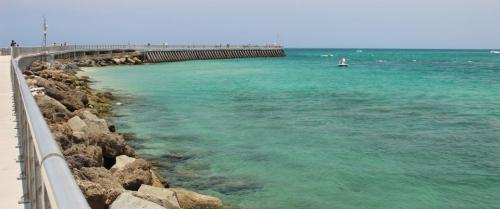 A scenic view of a pier extending into turquoise waters, with rocky shores and a clear sky in the background.