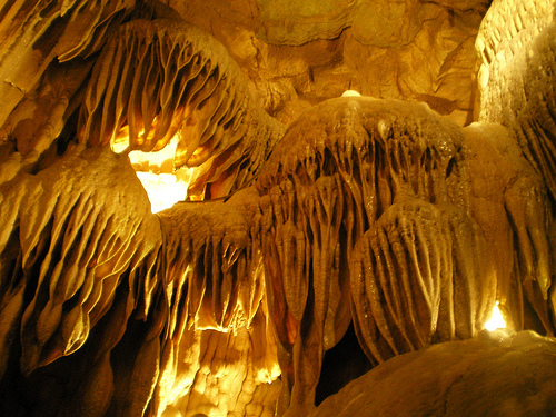 Stalactites and stalagmites in a cave, illuminated by warm light, creating a dramatic, textured rock formation.