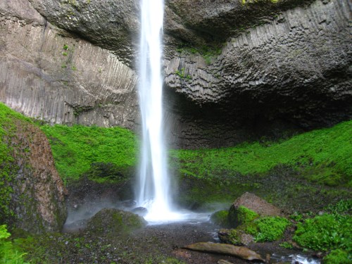 A waterfall cascades down rocky cliffs, surrounded by lush green vegetation and mossy stones.