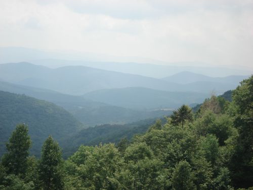 A panoramic view of rolling green mountains under a cloudy sky, showcasing layers of hills in the distance.