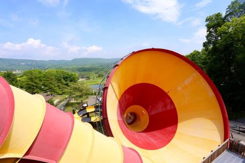 A colorful water slide spirals down into a scenic landscape with trees and mountains in the background.