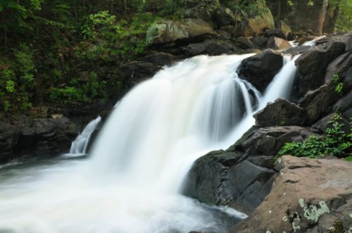 A serene waterfall cascades over rocky terrain, surrounded by lush greenery and soft mist.