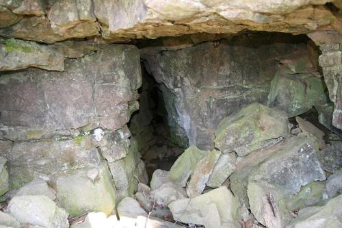 A rocky cave entrance surrounded by moss-covered stones and debris.