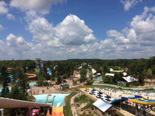 Aerial view of a water park with slides, pools, and lush greenery under a blue sky with fluffy clouds.