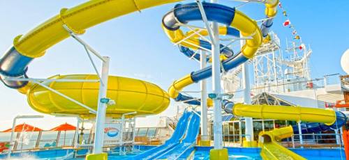 Colorful water slides on a cruise ship deck, with a clear blue sky and ocean in the background.