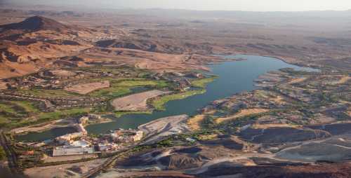 Aerial view of a desert landscape featuring a large lake surrounded by hills and sparse vegetation.