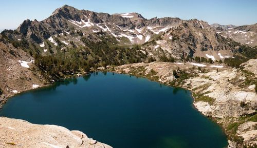 A serene mountain lake surrounded by rugged peaks and patches of snow under a clear blue sky.