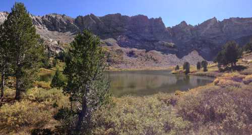 A serene mountain lake surrounded by rocky cliffs and lush greenery under a clear blue sky.