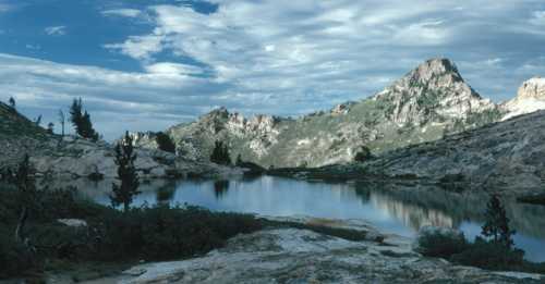 A serene mountain landscape with a reflective lake, rocky terrain, and dramatic clouds in the sky.