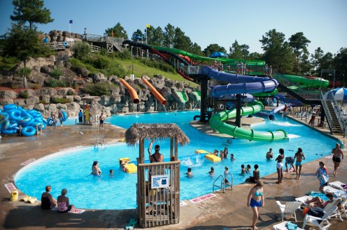 A vibrant water park scene with slides, a pool, and people enjoying the sun and water activities.