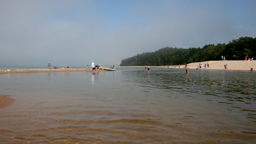 A serene beach scene with people enjoying the water, surrounded by trees and a misty sky.