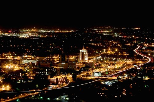 A nighttime cityscape with illuminated buildings and winding roads, showcasing a vibrant urban skyline.