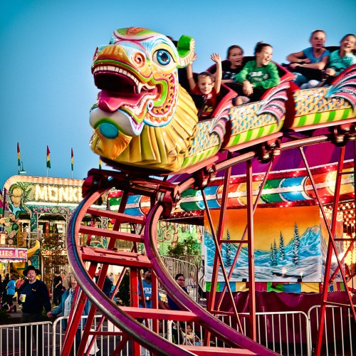 A colorful roller coaster with riders enjoying the ride at a lively carnival, surrounded by festive decorations.