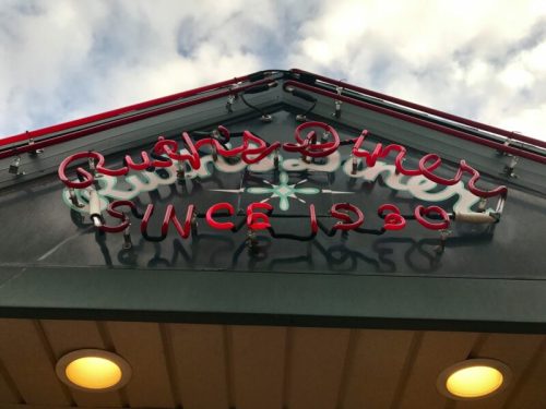 Neon sign of Bush's Diner, featuring the text "Bush's Diner Since 1930" against a cloudy sky.