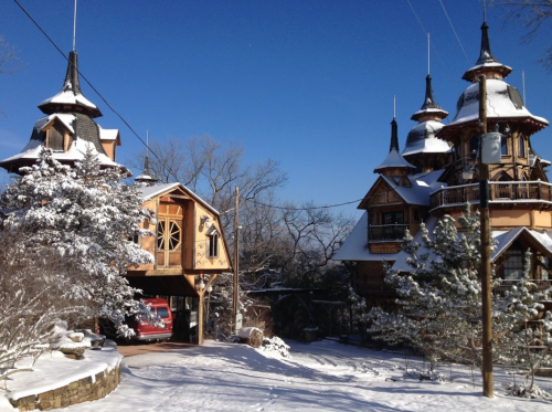 Two whimsical, turreted houses covered in snow, surrounded by trees under a clear blue sky.