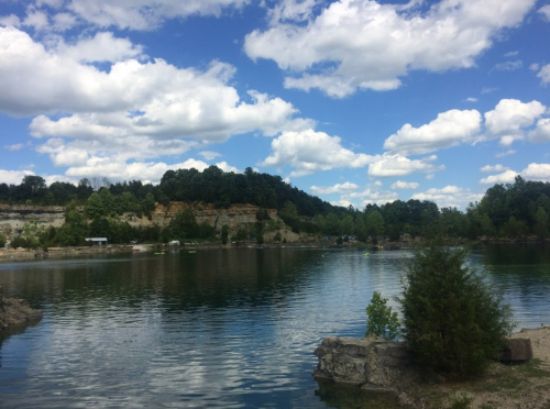 A serene lake surrounded by lush greenery and rocky cliffs under a partly cloudy sky.