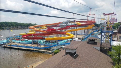 A vibrant water park with colorful slides, a lake, and people enjoying the attractions on a sunny day.