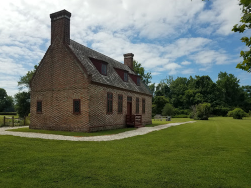 A historic brick house surrounded by green grass and trees under a partly cloudy sky.
