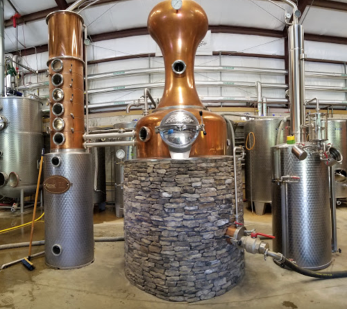 A copper and stainless steel distillation setup in a spacious industrial facility.