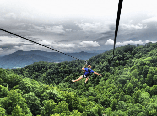 A person zip-lining over lush green mountains under a cloudy sky.