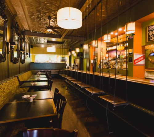 A cozy restaurant interior featuring wooden tables, a bar with stools, and decorative mirrors on the walls.