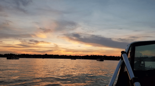A serene sunset over a lake, with boats silhouetted against the colorful sky and calm water.