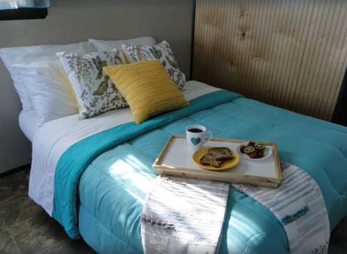 A cozy bedroom with a neatly made bed, colorful pillows, and a tray of cookies and coffee on the blanket.