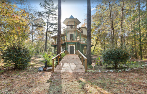 A unique, multi-level house surrounded by trees, with a wooden walkway leading to the entrance.