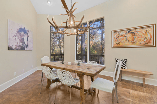 A modern dining room with a wooden table, stylish chairs, and large windows showcasing a natural view.