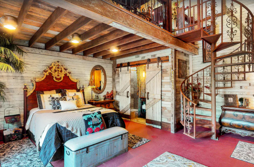 Cozy bedroom with wooden beams, a spiral staircase, and rustic decor, featuring a large bed and vintage furnishings.