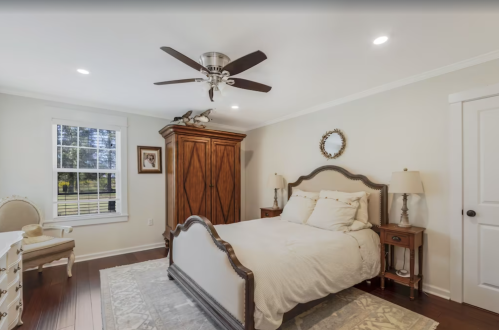 Cozy bedroom featuring a bed, wooden wardrobe, nightstands, and a ceiling fan, with soft lighting and neutral decor.