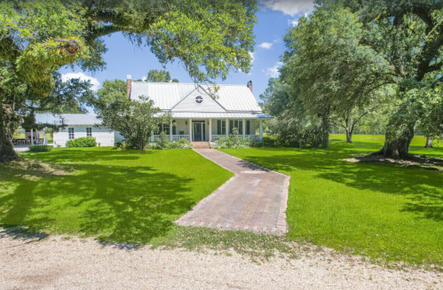 A charming house with a metal roof, surrounded by lush green grass and trees, with a brick pathway leading to the entrance.
