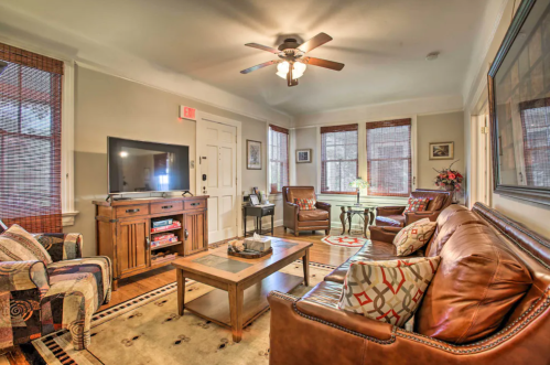 Cozy living room with a TV, leather sofas, a wooden coffee table, and large windows with blinds. Warm, inviting decor.