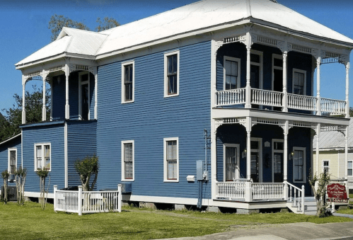 A large blue two-story house with white trim, featuring balconies and a well-maintained lawn.