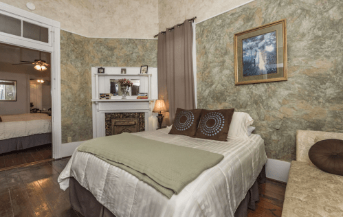 Cozy bedroom with a bed, decorative pillows, a fireplace, and green textured walls. A warm, inviting atmosphere.