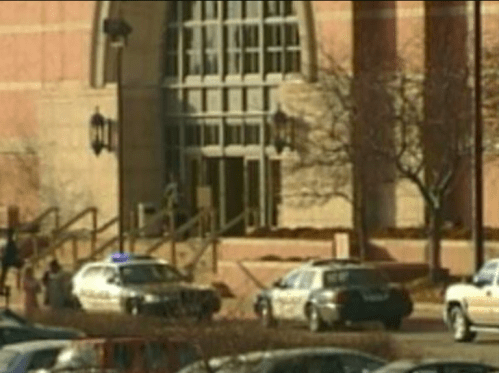 Two police cars parked outside a building, with people walking near the entrance.