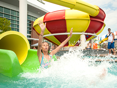 A girl splashes into a pool after sliding down a colorful water slide on a sunny day.