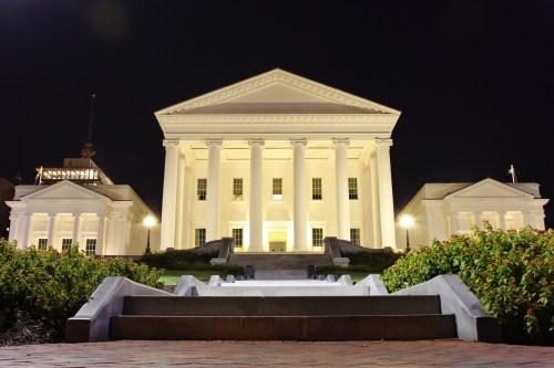 The Virginia State Capitol illuminated at night, showcasing its grand columns and surrounding gardens.