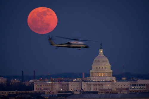 A helicopter flies near the U.S. Capitol, with a large, glowing full moon in the background at dusk.