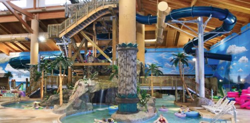 Indoor water park featuring slides, a lazy river, palm trees, and a tropical-themed environment.