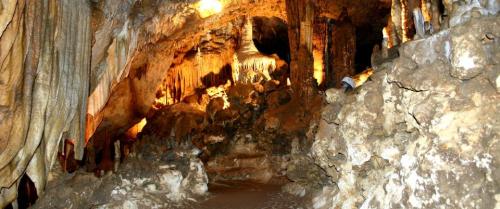A dimly lit cave interior featuring stalactites, stalagmites, and rocky formations along a winding path.