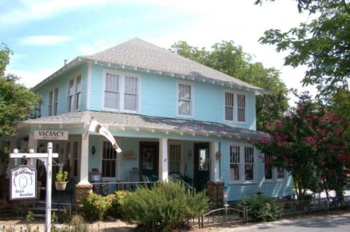 A charming blue bed and breakfast with a welcoming porch and a "Vacancy" sign, surrounded by greenery.