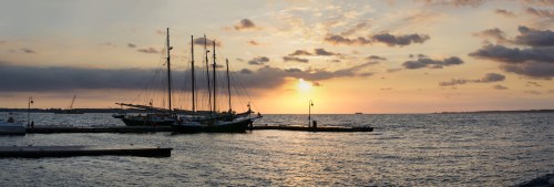 A sailboat docked at sunset, with vibrant colors reflecting on the water and clouds in the sky.