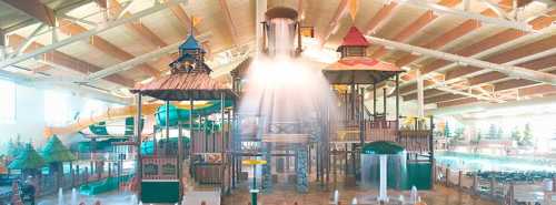 Indoor water park featuring colorful play structures, slides, and water features under a spacious roof.