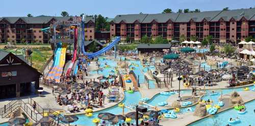 A vibrant water park with slides, pools, and sunbathers, surrounded by a hotel and lush greenery.