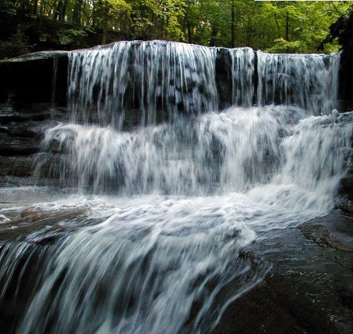 A serene waterfall cascading over rocks, surrounded by lush green trees in a tranquil forest setting.
